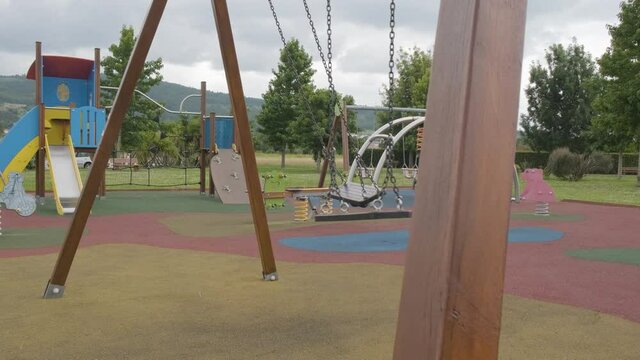 Empty abandoned children's playground on gloomy day, swings swinging