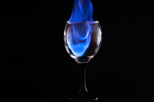 Picture of a burning glass cup set on fire with the help of medicinal alcohol, on a reflective surface, on a black background, having reflection