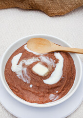 Traditional African sorghum porridge in white bowl with melting butter and wooden spoon with copy space
