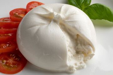 Fresh piece burrata cheese close up on white background with tomato slices and basil leaves 