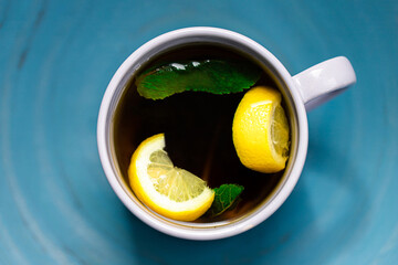 Black tea with lemon and mint in a white mug on a blue background. Top view.