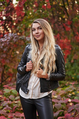 beautiful young woman with long white hair in leather clothes on a background of red and yellow foliage. autumn portrait