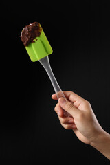 Chef holding spatula and melted chocolate on black background