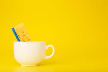 Creative, minimal dishwashing concept, yellow cleaning sponge in white ceramic cup on yellow background with copy space
