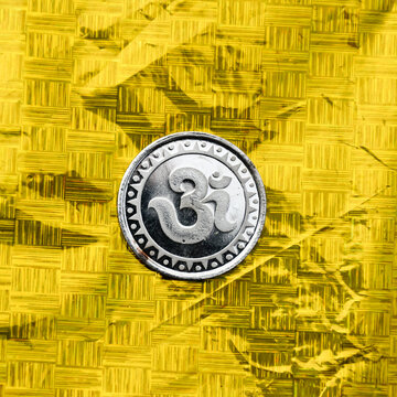 Silver Coin embossing with sacred spiritual symbol Om or Aum on golden backgrounds.