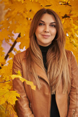 Naklejka na ściany i meble young beautiful woman stands next to beautiful autumn yellow foliage