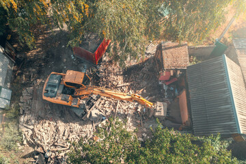 Process of demolition building dismantling aerial top view. Excavator breaking house.