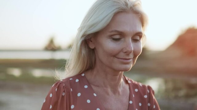 Close-up view of positive woman looking to the sides and walking on the field at sunset