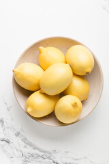 Naklejka na ściany i meble Several yellow bright lemons in a plate on a light background. Bright citruses.