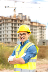 A handsome builder in glasses and a protective helmet stands against the background of a construction site.