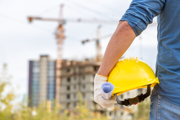 close-up of a construction worker with a safety helmet in his hand against the backdrop of a...