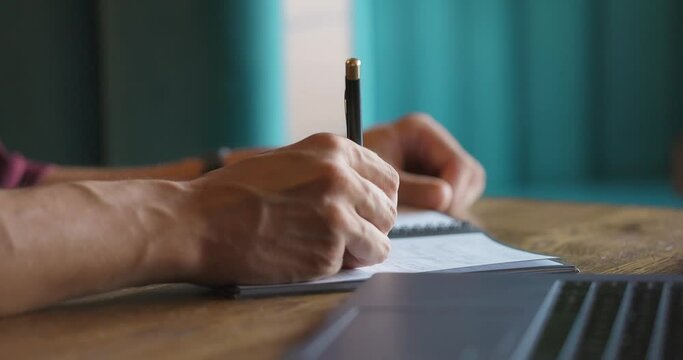 Close-up shot of hands of unrecognizable men writing down in notepad while sitting at cafe table. Slow motion