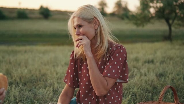 Positive blond middle-aged woman eating cookie at picnic