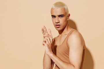 Side view young sexy twink blond latin hispanic gay man with make up in beige tank shirt hold hands...