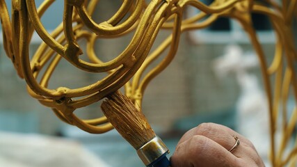 A woman's hand paints metal products with gold paint, close-up