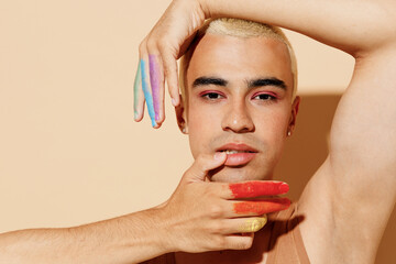 Young serious sexy trendy blond latin gay man with make up fingers painted in rainbow flag colors...