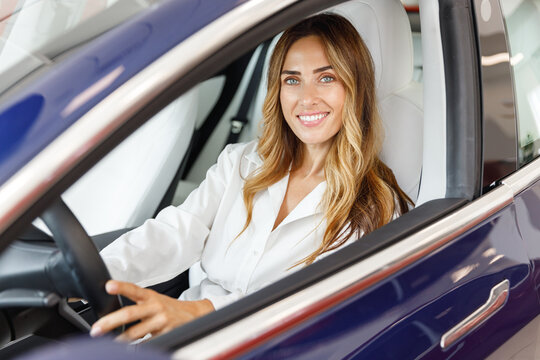 Smiling driver woman customer buyer client in shirt hold put hand on steering wheel choose auto want buy new automobile in car showroom vehicle salon dealership store motor show indoor. Sales concept.