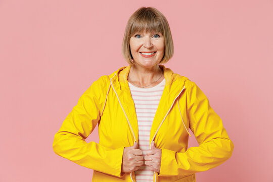 Happy Mature Elderly Senior Lady Woman 55 Years Old Wear Yellow Waterproof Raincoat Outerwear Isolated On Plain Pastel Light Pink Background Studio Portrait. Outdoors Wet Fall Weather Season Concept.