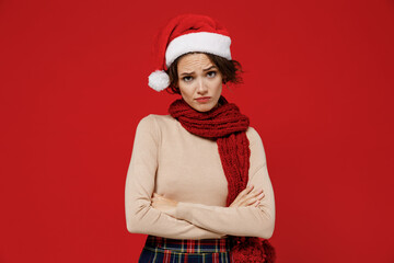 Young shrewd caucasian woman 20s wearing Santa Claus Christmas red hat hold hands crossed folded look camera isolated on plain red background studio portrait. Happy New Year 2022 celebration concept