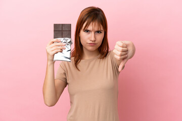 Redhead girl isolated on pink background taking a chocolate tablet making bad signal