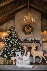 young beautiful woman model with long hair in a beige suit christmas tree christmas In brown wooden houses 