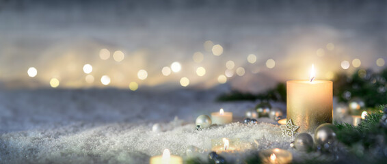 Christmas decoration with candle, lights, fir branches and ornaments on snow, panoramic format
