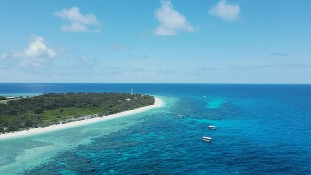 Lush island location surrounded by tropical blue ocean waters and a underwater reef system. Drone view