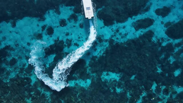 Unique view of a dive boat as it maneuvers through the water over a tropical reef system. High drone view