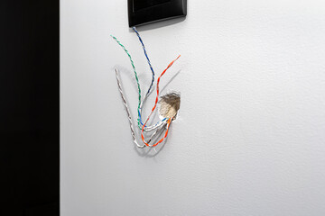 Eight colored cables from the intercom stick out from the wall of the house in the room.
