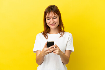 Redhead girl isolated on yellow background sending a message or email with the mobile