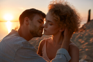 Two young people in love, couple looking passionate, kissing each other on the beach at sunset