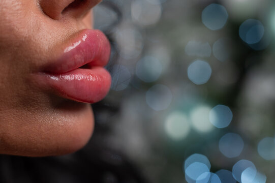 Close-up of large plump female lips against a background of christmas decorations.
