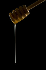 Honey dipper with golden honey dripping off, low key