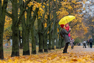 Mother holds small child and large yellow umbrella in her arms. Walk in the autumn park.
