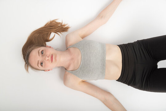 Young woman in sports top and leggings lies on white floor after training. Top view. Portrait on white background.