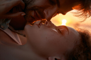 Closeup of young man and woman in love kissing on sunset while relaxing together outdoors