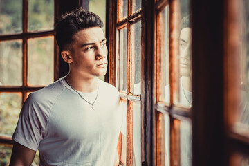 Serious and thoughtful young boy teenager looking outside the windows at home. Concept of youthful people and 18 age people problems and lifestyle © simona