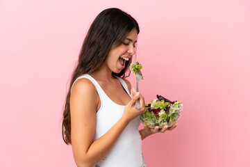 Young caucasian woman isolated on pink background holding a bowl of salad and looking at it with happy expression