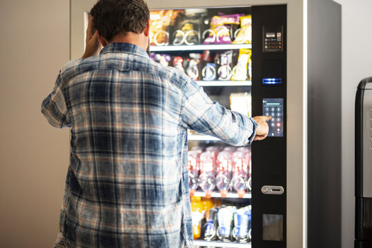 Hipster style man viewed from back buying snacks or drink from vending automatic machine typing product code. People and travel concept lifestyle