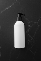 Lotion white plastic bottle on black marble desk background, vertical. Luxury cosmetic beauty product template for branding, top view. Container with pump mockup for skin care