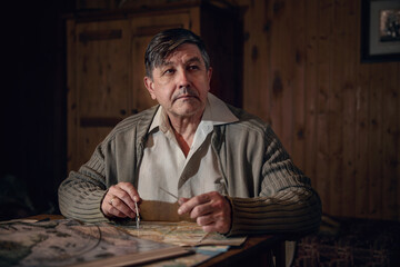 An aged man is sitting alone at a table in front of an old map of military operations, restoring the course of historical events. Cinematic style, film grain.