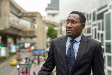 Portrait of handsome African businessman thinking in city