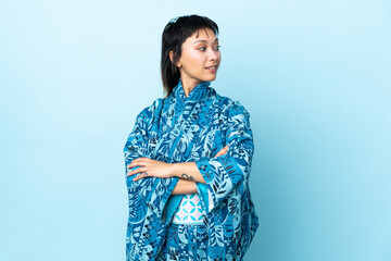 Young woman wearing kimono over isolated blue background looking to the side and smiling