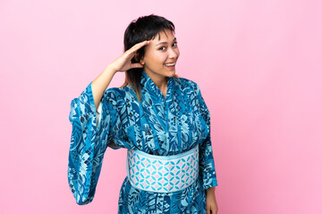 Young woman wearing kimono over isolated blue background listening to something by putting hand on the ear