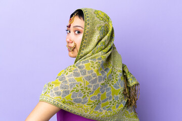 Indian woman isolated on purple background in back position and looking side