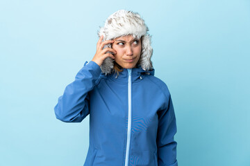 Young Uruguayan girl with winter hat isolated on blue background having doubts and with confuse face expression