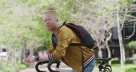 Portrait of smiling albino african american man with dreadlocks in park with bike looking at camera - Powered by Adobe