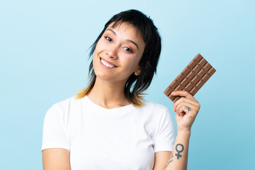 Young Uruguayan woman over isolated blue background taking a chocolate tablet and happy