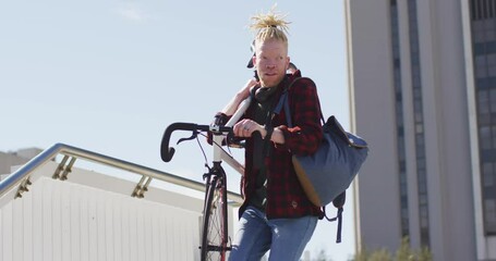 Thoughtful albino african american man with dreadlocks going down stairs with bike - Powered by Adobe