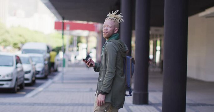 Thoughtful albino african american man with dreadlocks walking on street using smartphone